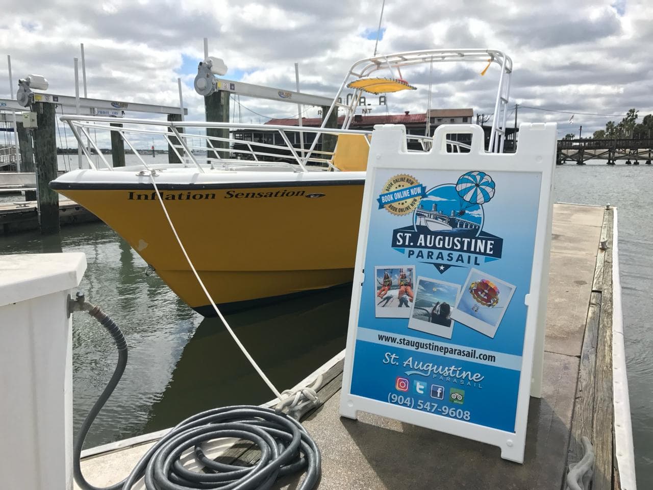 The parasail boat Inflation Sensation tied up at the St. Augustine Municipal Marina beside the St. Augustine Parasail dock sign.